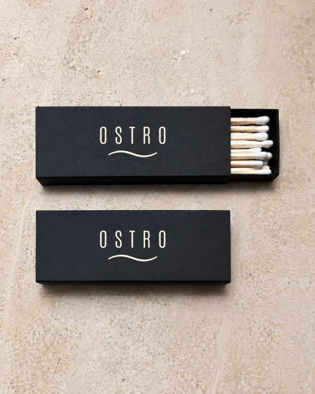 Two black slim matchboxes printed with an ivory bar wordmark, one tray open, an example brand