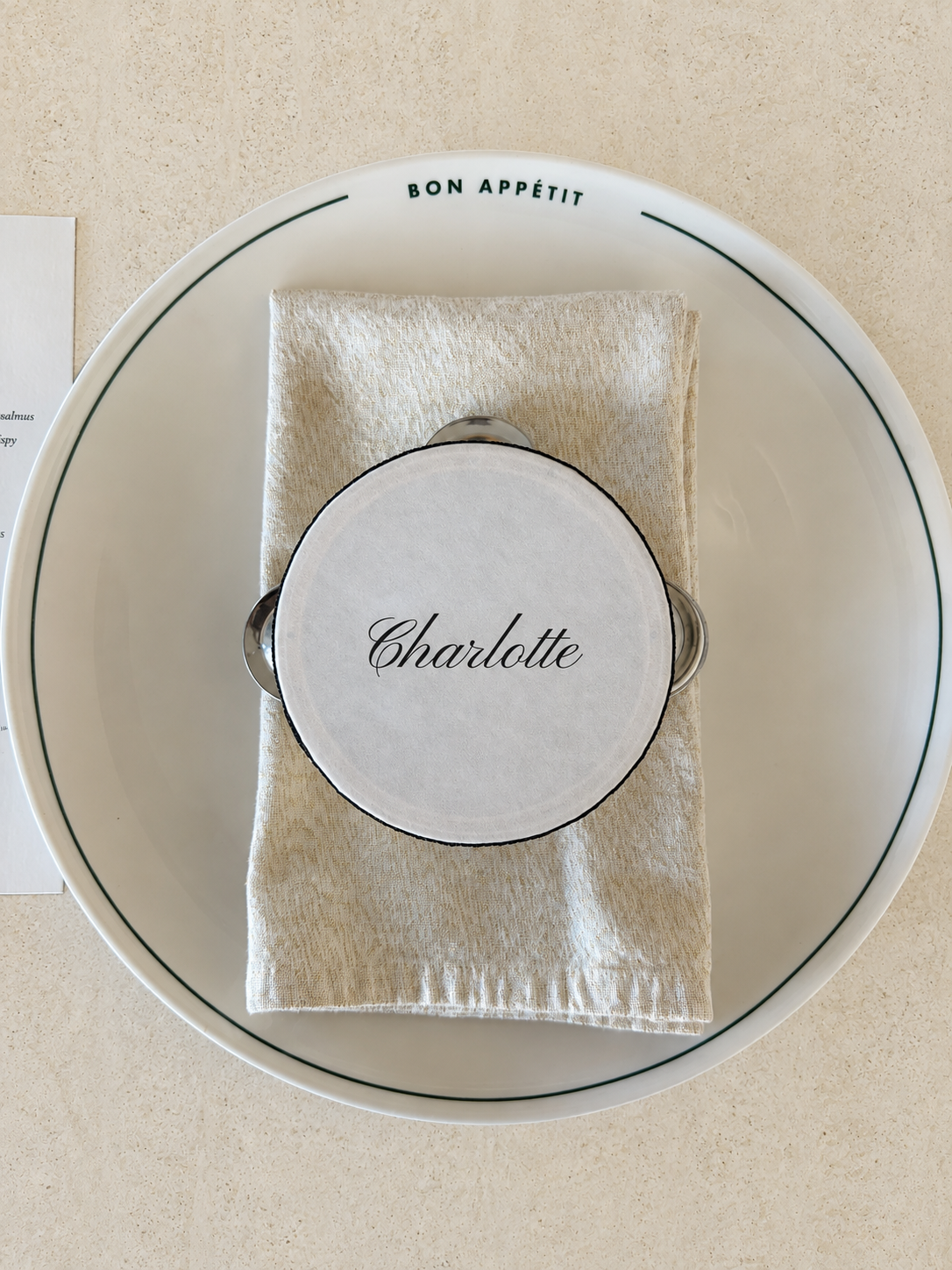 Personalised tambourine place card resting on a folded napkin at a table setting