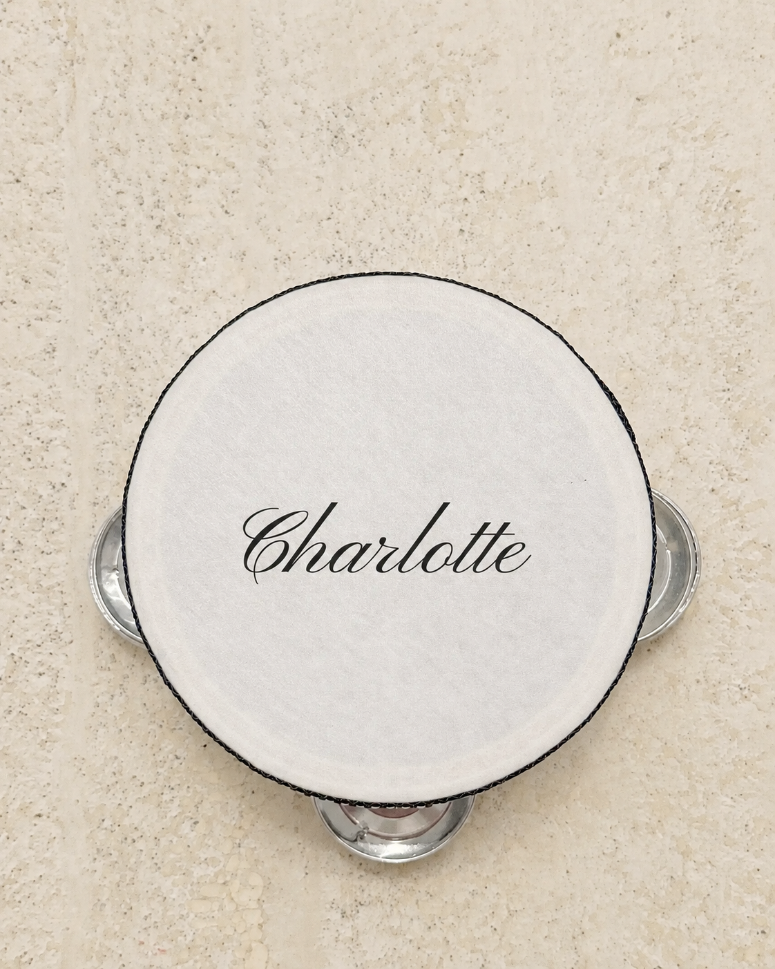 Personalised four inch tambourine place card printed with a guest name in navy script, on pale stone