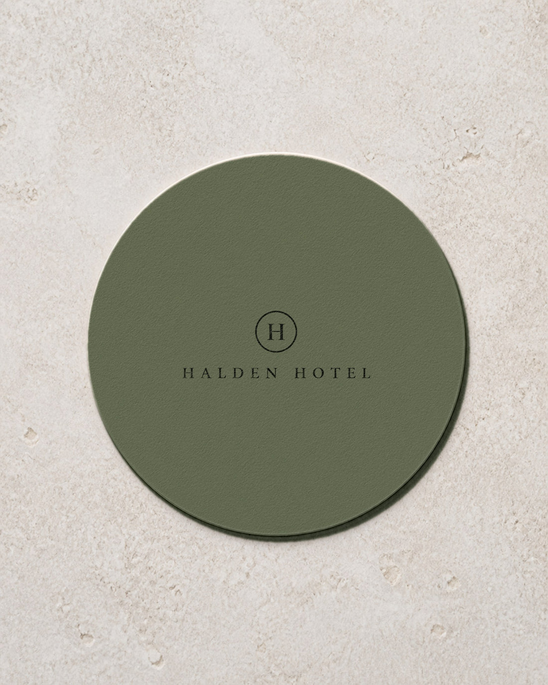 Round sage green coaster printed with a hotel mark in black, an example brand