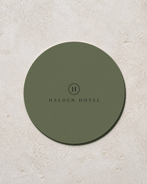 Round sage green coaster printed with a hotel mark in black, an example brand
