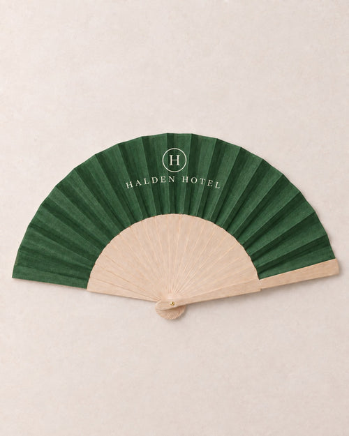 Branded folding fan on plain bamboo ribs, printed edge to edge in deep green with a hotel mark in ivory, an example brand