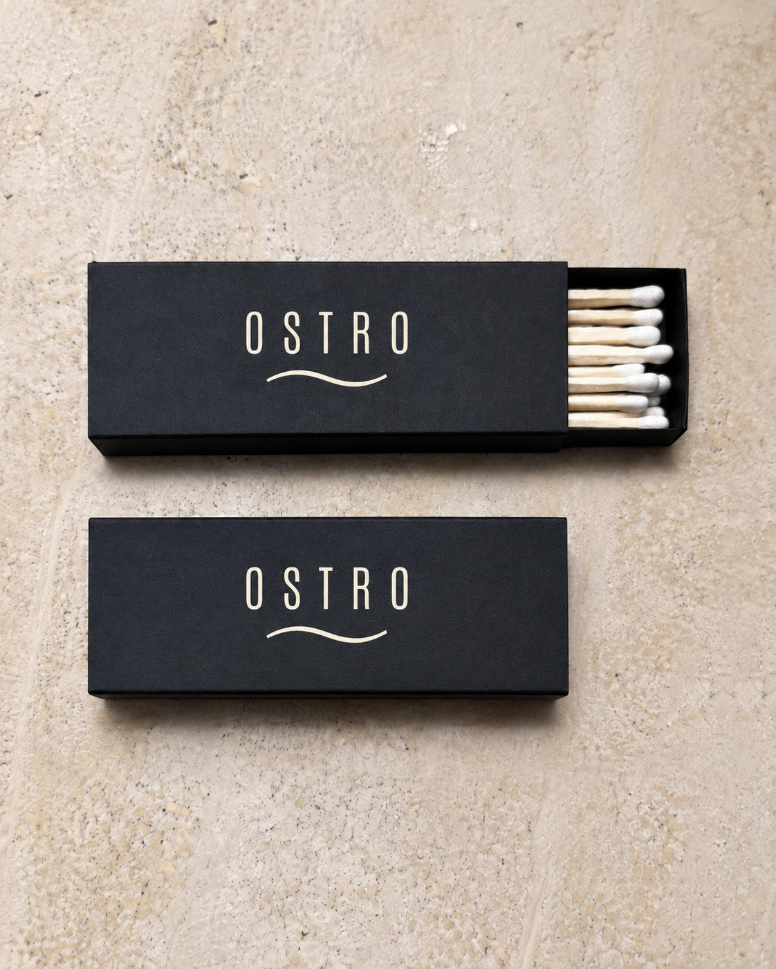 Two black slim matchboxes printed with an ivory bar wordmark, one tray open, an example brand