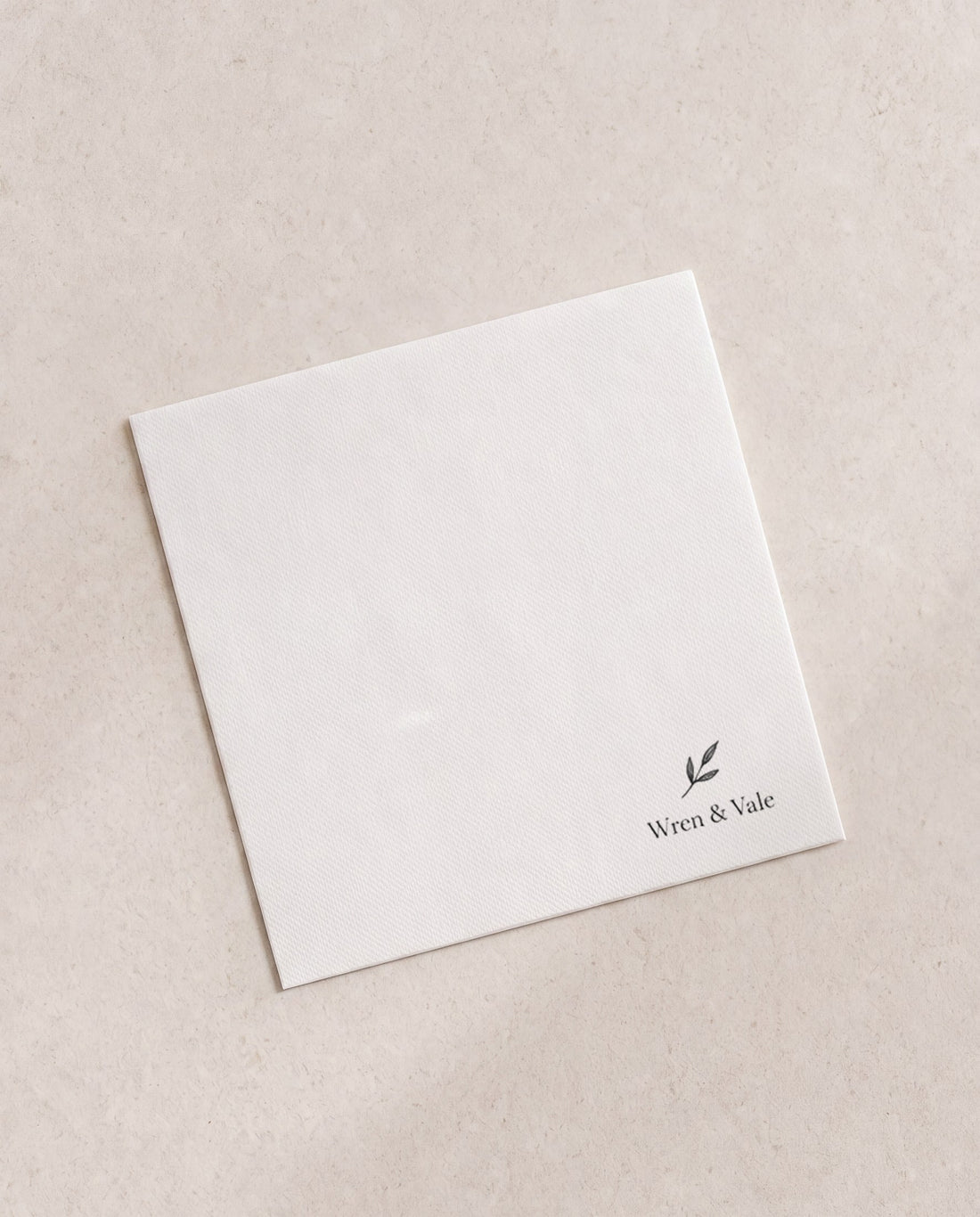 Folded white cocktail napkin printed in black with a small winery mark in the corner, an example brand