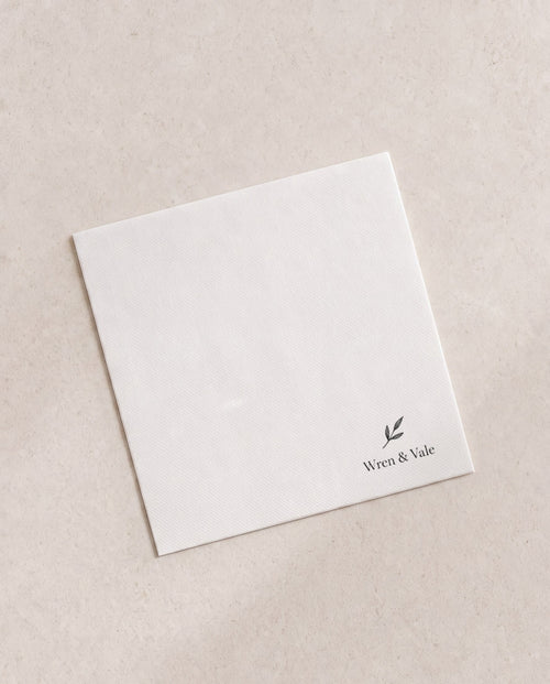 Folded white cocktail napkin printed in black with a small winery mark in the corner, an example brand