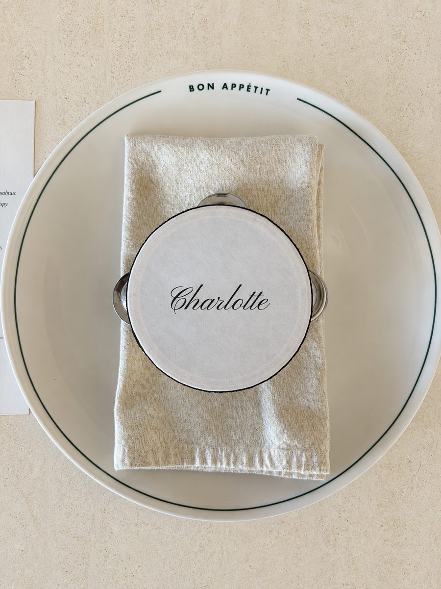 Personalised tambourine place card resting on a folded napkin at a table setting