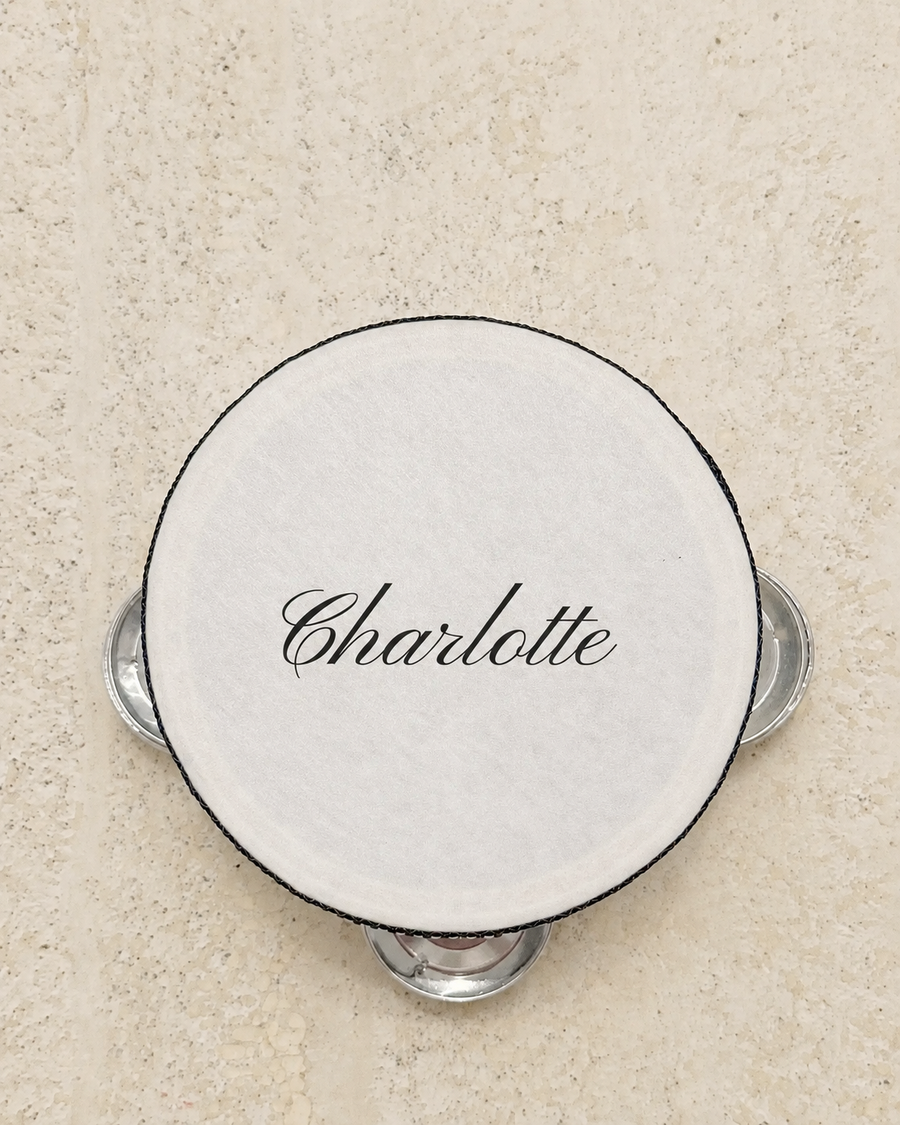 Personalised four inch tambourine place card printed with a guest name in navy script, on pale stone
