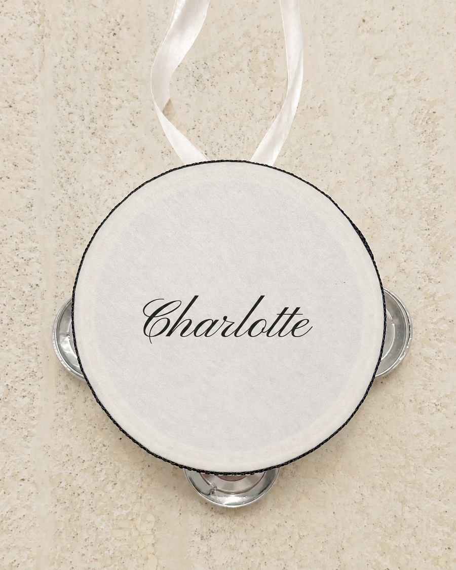 Personalised four inch tambourine place card tied with an ivory ribbon, on pale stone