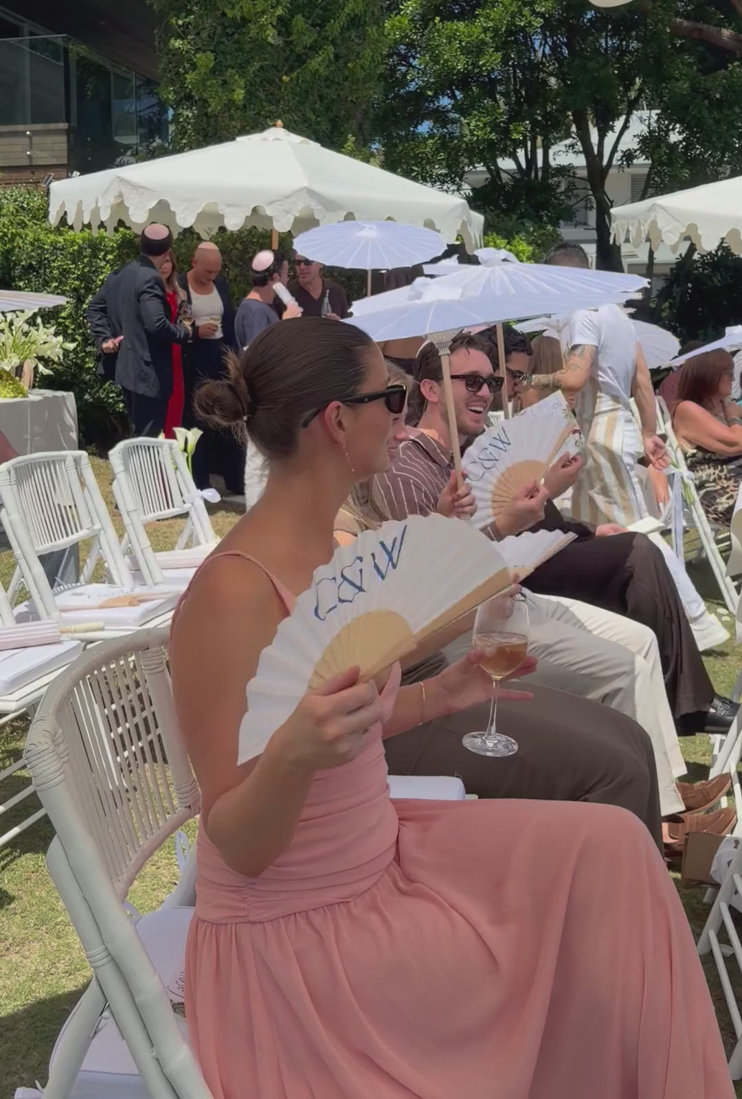 A seated guest holding a personalised Solene fan at an outdoor wedding ceremony