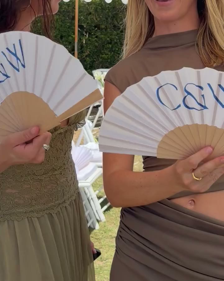 Monogrammed hand fans held by two guests